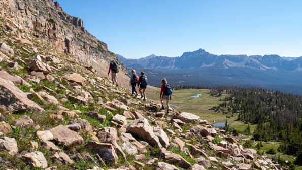 A guide leads three clients to a rock climbing wall in the Uinta Mountains