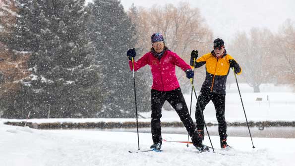 Two Nordic skiers skate ski through falling snow in Park City, UT