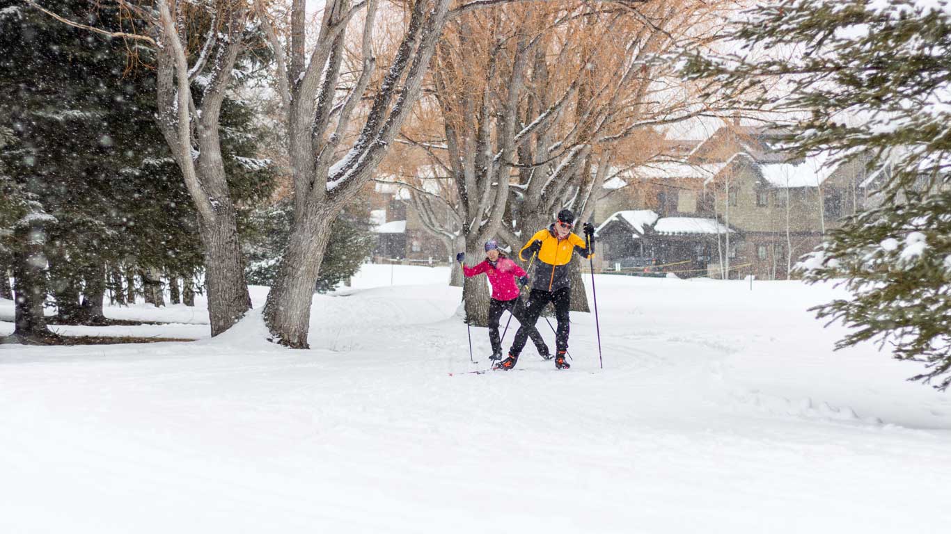 Two skiers skate ski through falling snow in Park City, UT