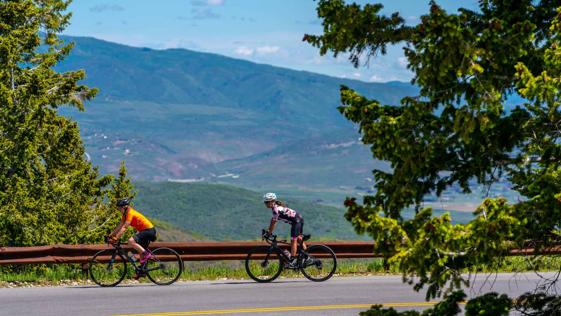 Two road bikers ride on a road overlooking Park City, UT