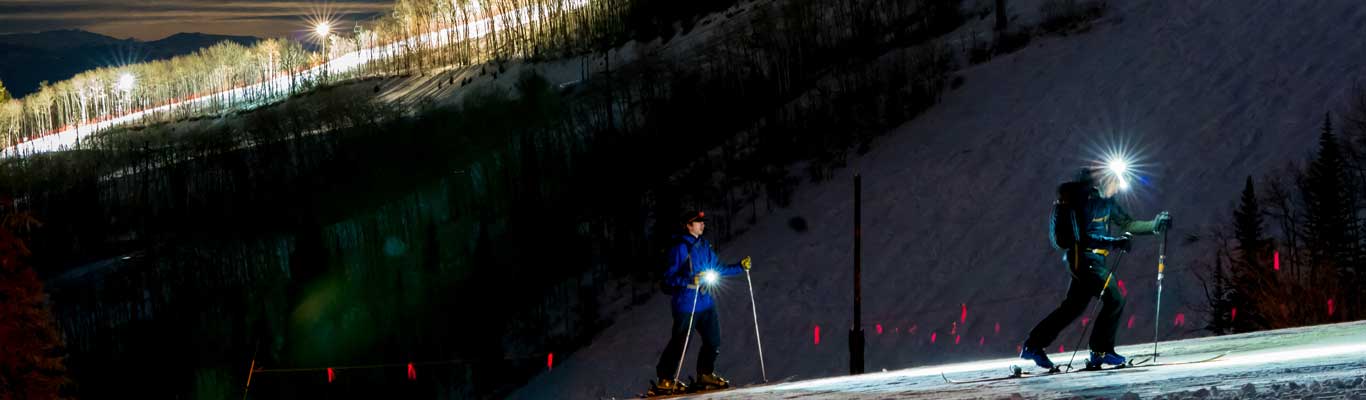Two skiers tour at night on Park City Mountain Resort under a full moon.