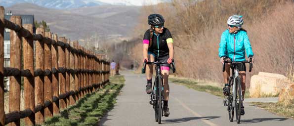 Two road cyclists ride a paved bike path in Park City, UT