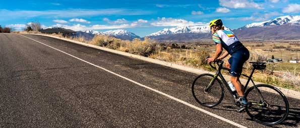 A cyclist rides up a steep road overlooking the snow-capped Wasatch mountains in Utah