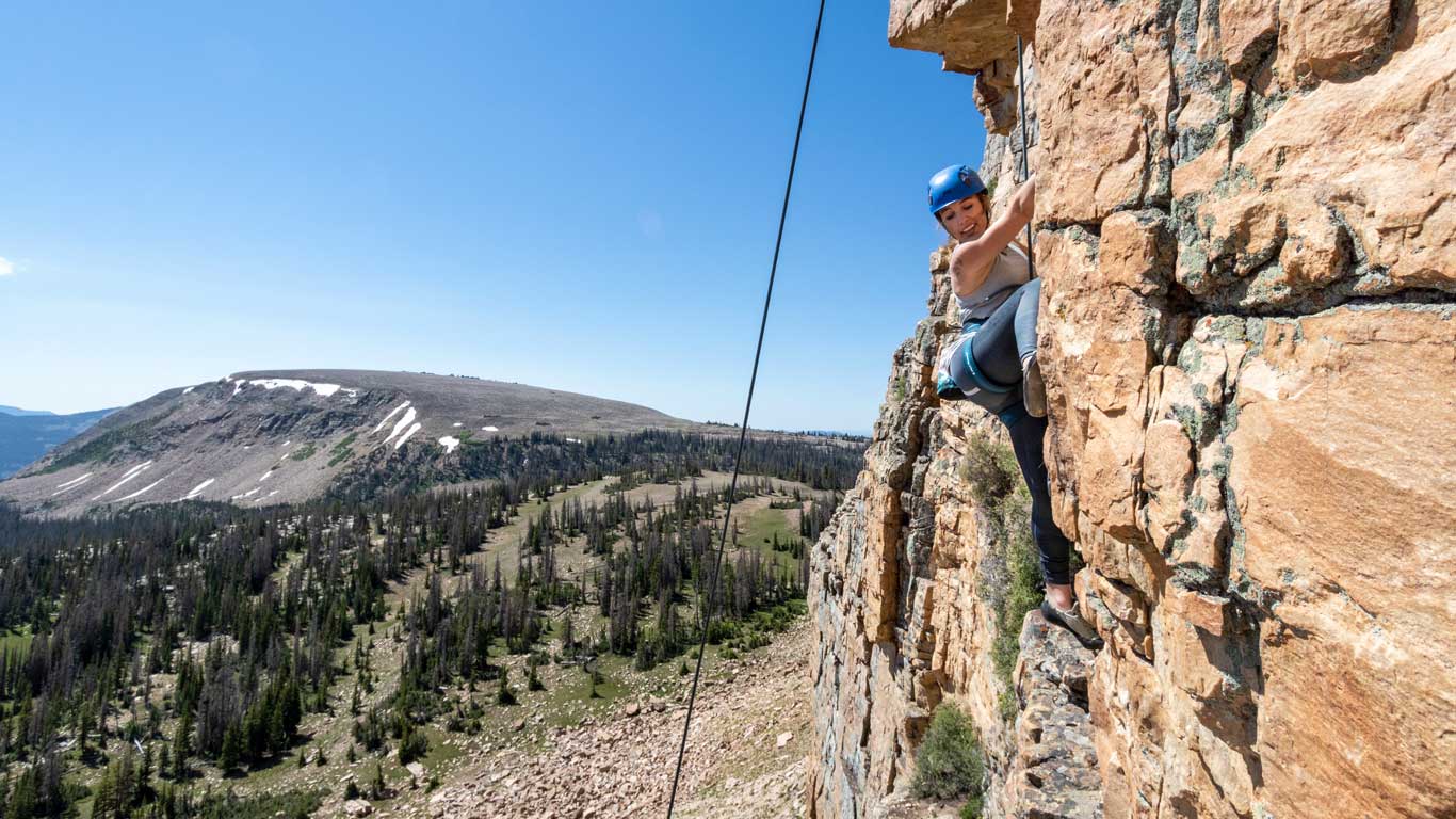 A climber on a rope and harness scales a rock wall in the Uinta Mountains near Park City, UT