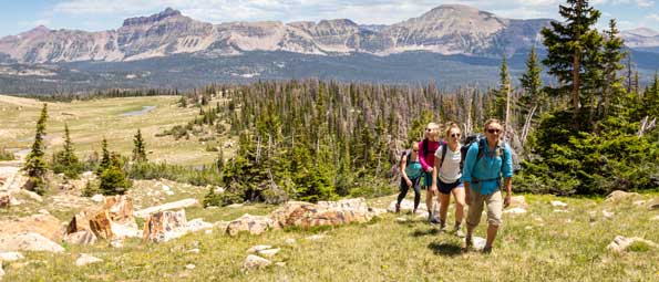 A guide leads three hikers on a trail overlooking the Uinta mountain range near Park City, UT